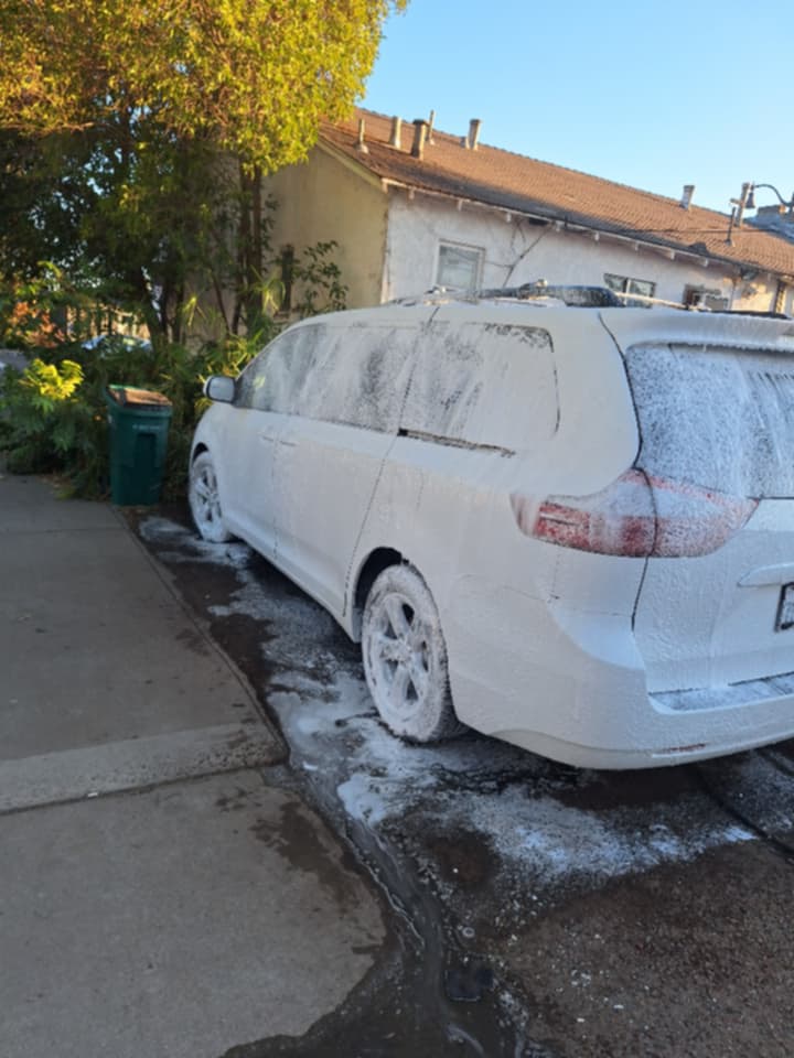 Minivan Toyota Sienna cubierta de espuma durante un lavado a domicilio al atardecer